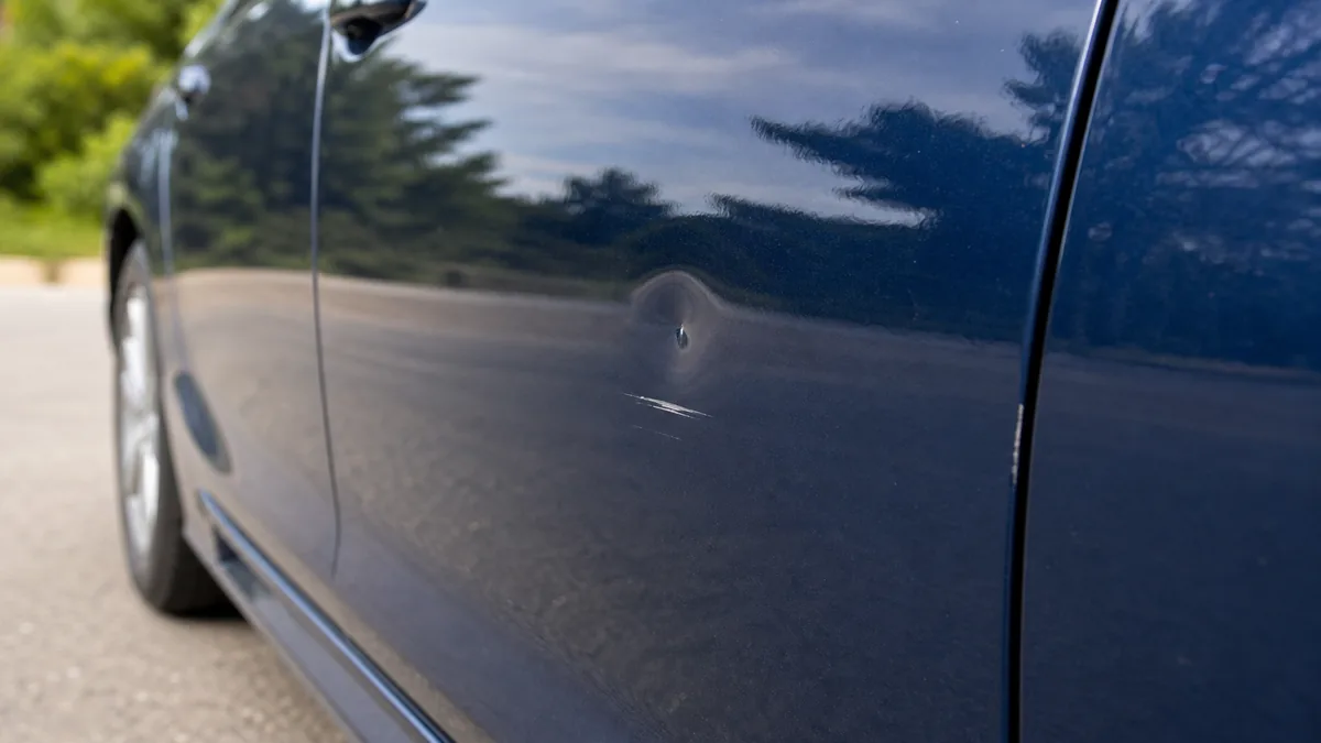 Door ding and paint scratch on a blue car door panel